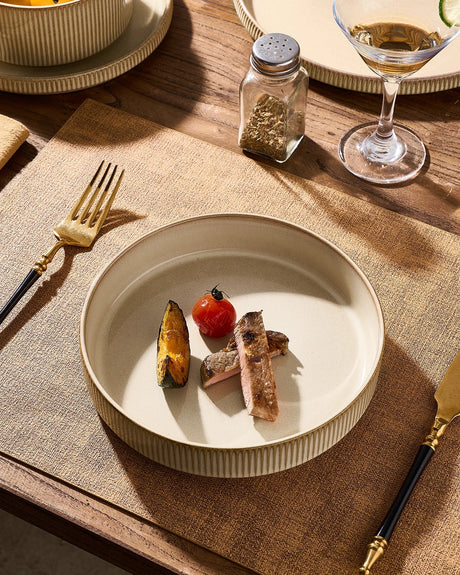 A cream-colored ribbed ceramic bowl holding a meal on a dining table.
