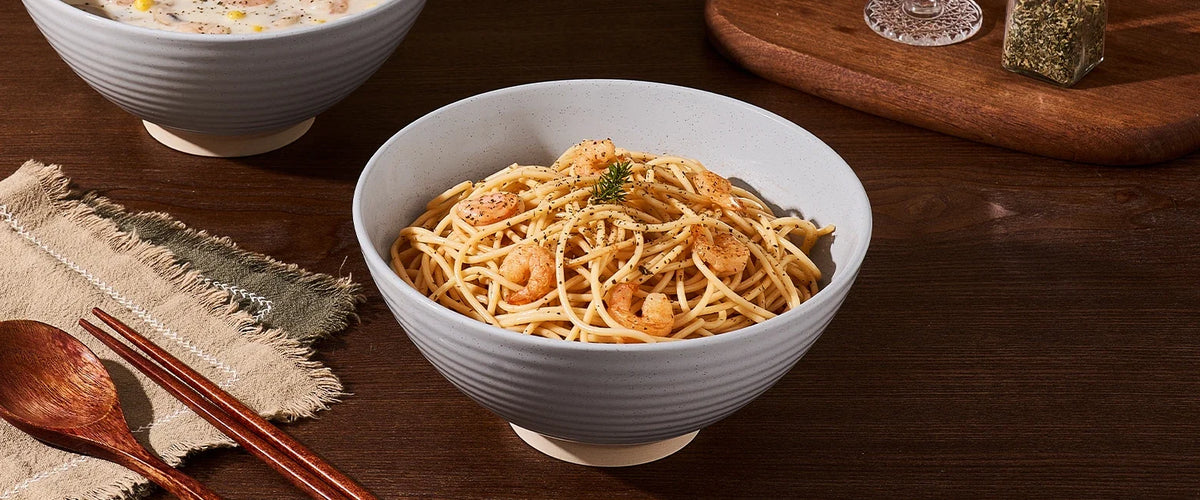 Speckled ceramic pasta bowl filled with shrimp pasta on a wooden table
