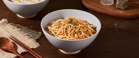 Speckled ceramic pasta bowl filled with shrimp pasta on a wooden table