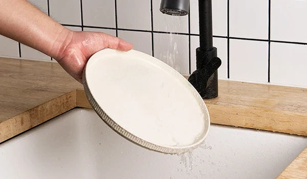 Ceramic dinner plate being rinsed over a kitchen sink