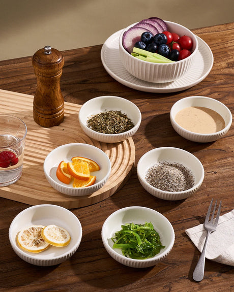 Small white ceramic dishes holding a sauce, herbs, citrus slices, and other accompaniments