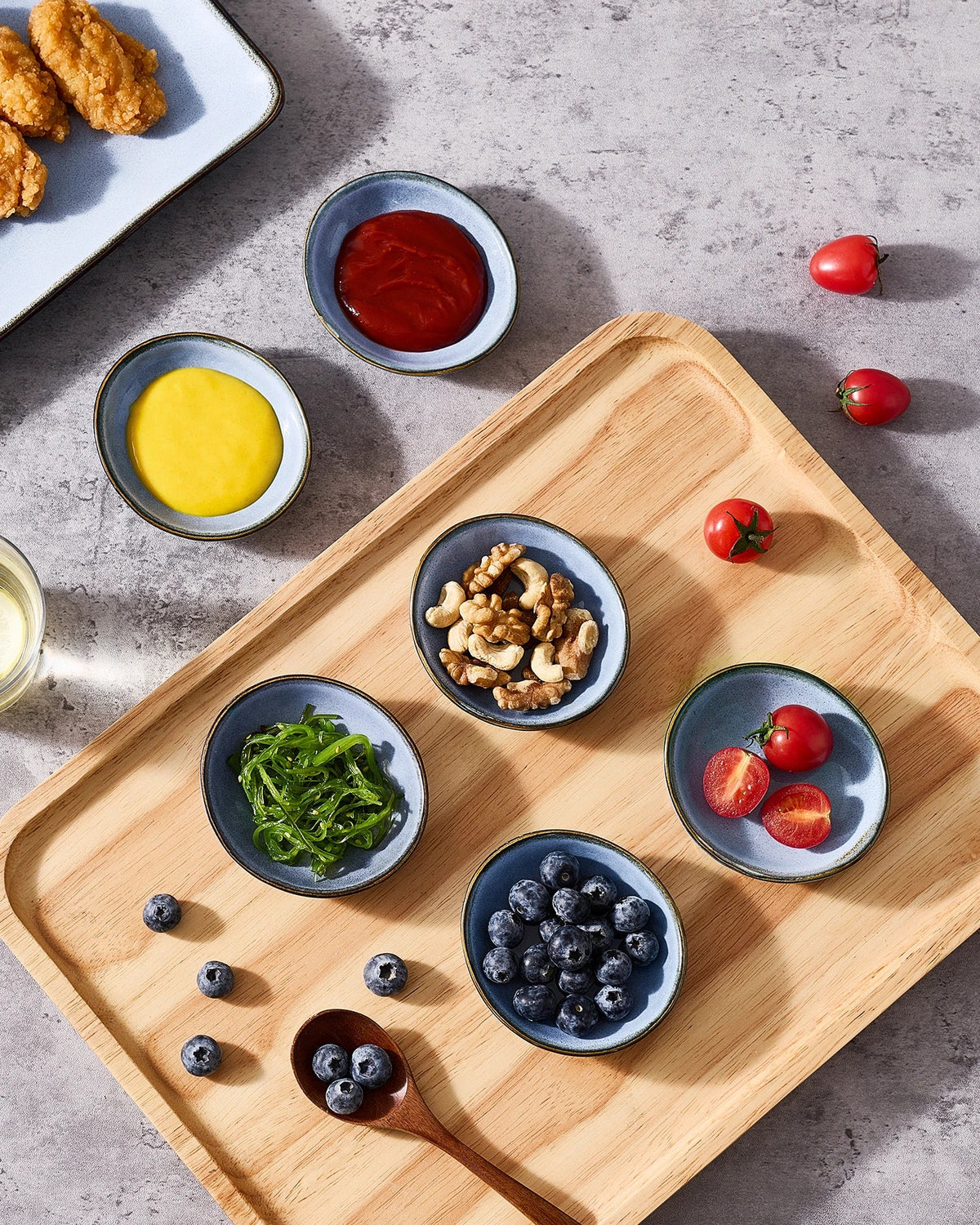 Small blue ceramic dishes holding sauces, berries, nuts and vegetables